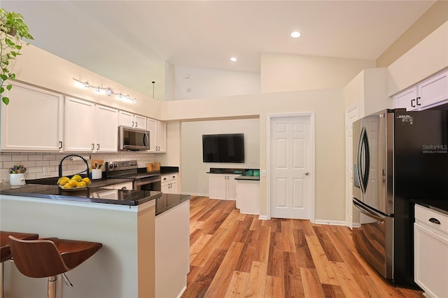 kitchen featuring light wood-type flooring, dark countertops, appliances with stainless steel finishes, white cabinets, and decorative backsplash