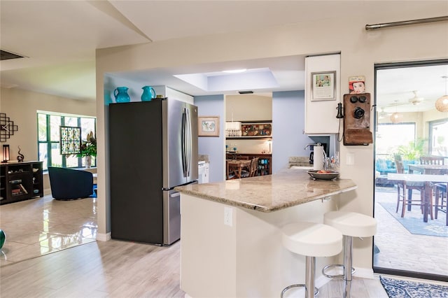 kitchen featuring light wood-type flooring, stainless steel refrigerator, a raised ceiling, kitchen peninsula, and a breakfast bar area