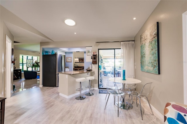 interior space featuring a wealth of natural light, kitchen peninsula, stainless steel refrigerator, and a kitchen breakfast bar