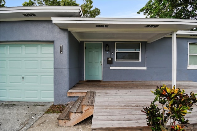 doorway to property with visible vents, an attached garage, and stucco siding