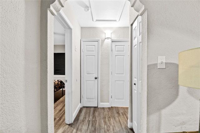 hallway featuring attic access, a textured wall, baseboards, and wood finished floors