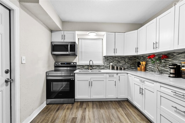 kitchen with appliances with stainless steel finishes, backsplash, a sink, and wood finished floors