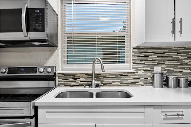 kitchen featuring white cabinets, backsplash, light stone countertops, stainless steel appliances, and sink