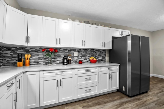 kitchen with tasteful backsplash, light countertops, dark wood-type flooring, freestanding refrigerator, and white cabinetry