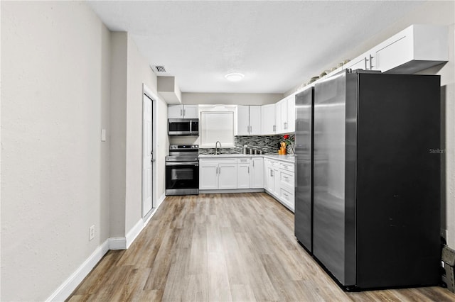 kitchen featuring light hardwood / wood-style flooring, tasteful backsplash, stainless steel appliances, sink, and white cabinetry