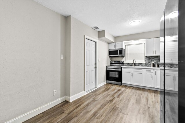 kitchen with backsplash, wood-type flooring, appliances with stainless steel finishes, sink, and white cabinetry