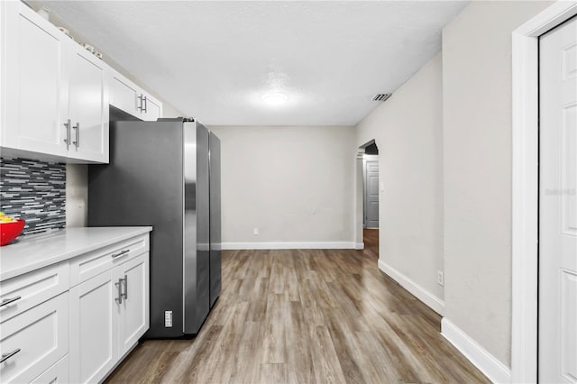 kitchen featuring stainless steel refrigerator, a textured ceiling, white cabinetry, light hardwood / wood-style flooring, and tasteful backsplash