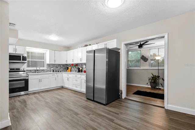 kitchen with wood-type flooring, stainless steel appliances, decorative backsplash, white cabinetry, and ceiling fan