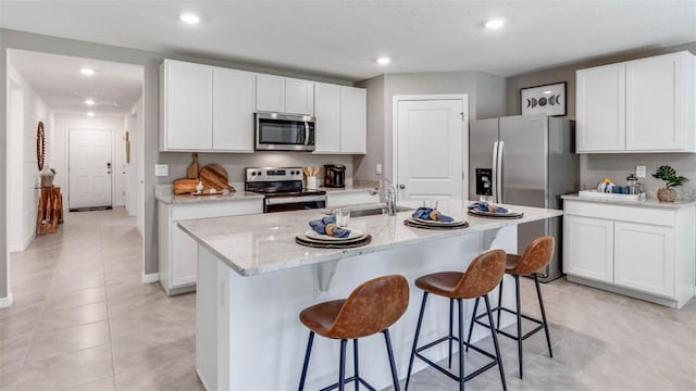 kitchen featuring a center island with sink, a kitchen bar, appliances with stainless steel finishes, and white cabinetry