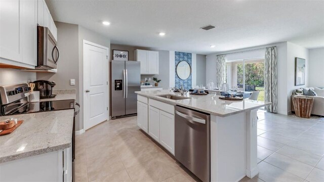 kitchen with white cabinetry, light stone counters, an island with sink, sink, and appliances with stainless steel finishes