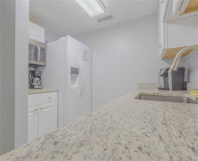 kitchen featuring light stone counters, white cabinets, white refrigerator with ice dispenser, and sink