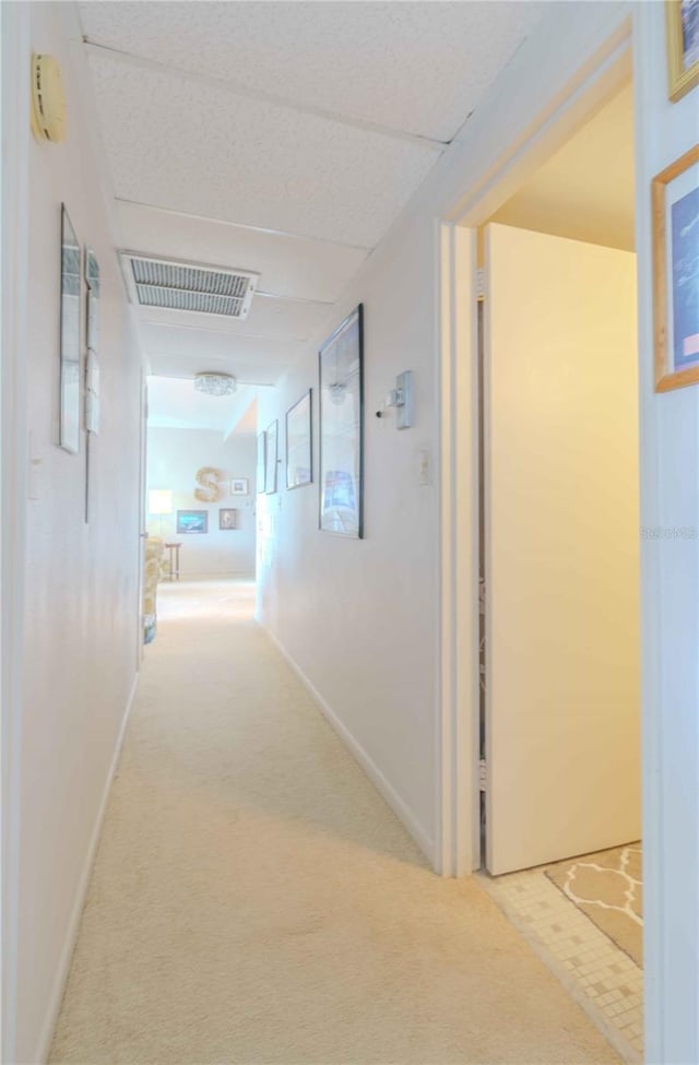 corridor with carpet, visible vents, a paneled ceiling, and baseboards