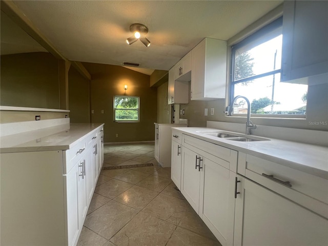 kitchen featuring vaulted ceiling, sink, light tile patterned floors, and white cabinetry