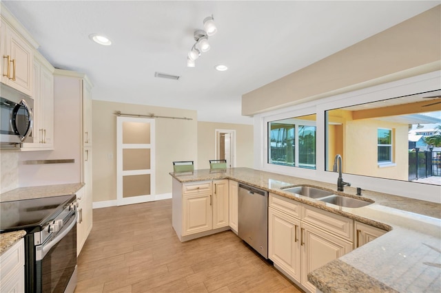 kitchen featuring sink, light stone counters, kitchen peninsula, light hardwood / wood-style floors, and appliances with stainless steel finishes