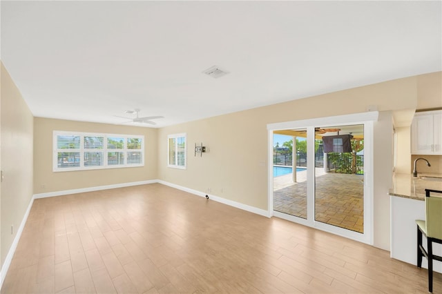 unfurnished living room with ceiling fan, a healthy amount of sunlight, light wood-type flooring, and sink