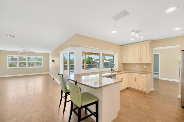 kitchen with ceiling fan, sink, light stone counters, kitchen peninsula, and a breakfast bar area