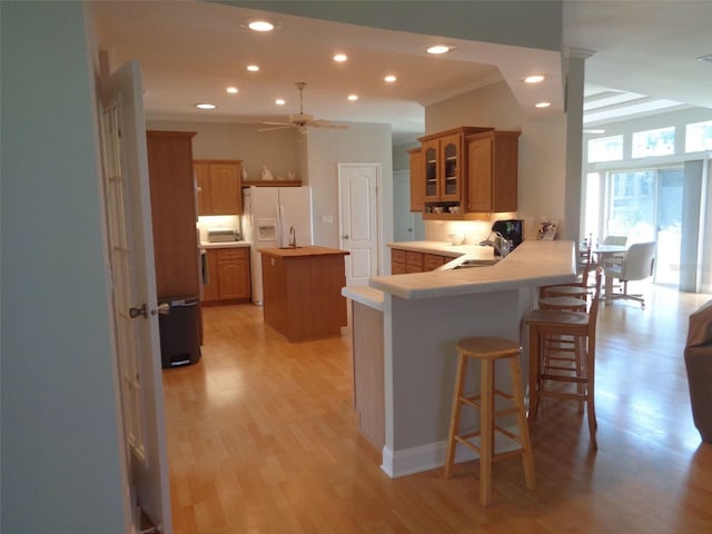 kitchen featuring light hardwood / wood-style flooring, decorative columns, kitchen peninsula, sink, and ceiling fan