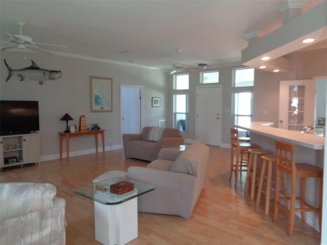 living room with light wood-type flooring, ceiling fan, indoor bar, and ornamental molding