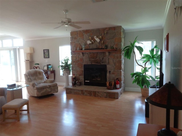 living room with crown molding, hardwood / wood-style flooring, a wealth of natural light, and a stone fireplace