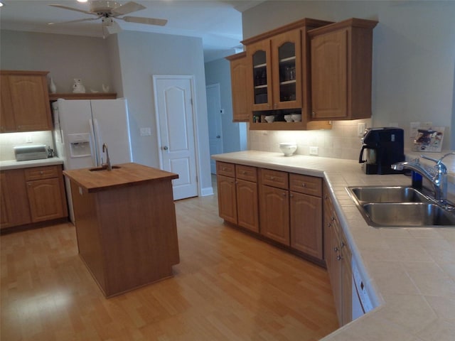 kitchen with light hardwood / wood-style flooring, white refrigerator with ice dispenser, sink, ceiling fan, and a kitchen island with sink