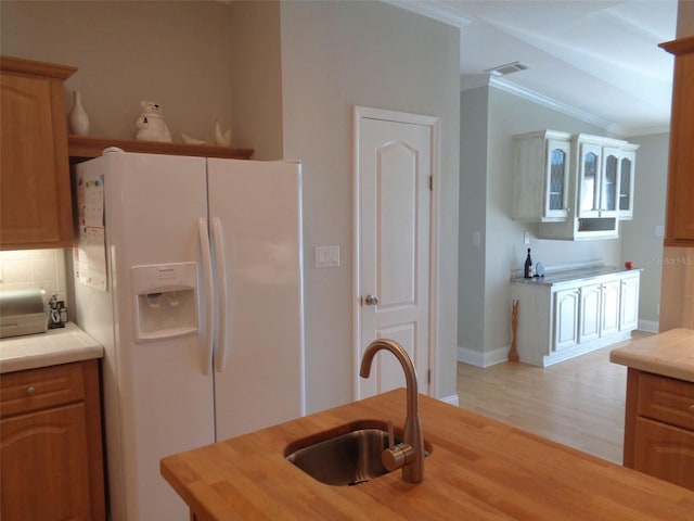 kitchen with white refrigerator with ice dispenser, tile counters, sink, and light wood-type flooring