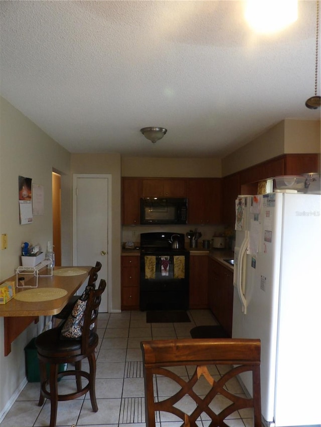 kitchen with freestanding refrigerator, black microwave, light countertops, light tile patterned floors, and stove