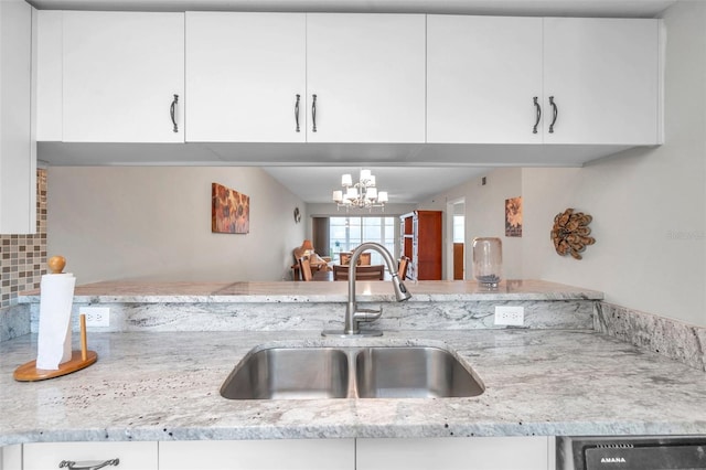 kitchen with white cabinets, a notable chandelier, light stone countertops, and sink