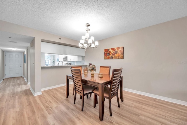 dining room with a textured ceiling, light hardwood / wood-style floors, and a chandelier