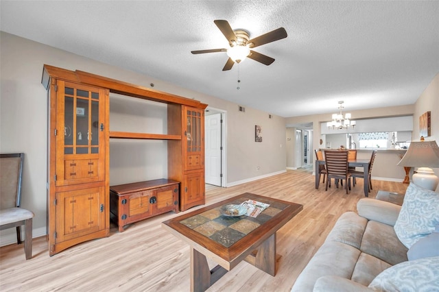 living room featuring ceiling fan with notable chandelier, light hardwood / wood-style floors, and a textured ceiling