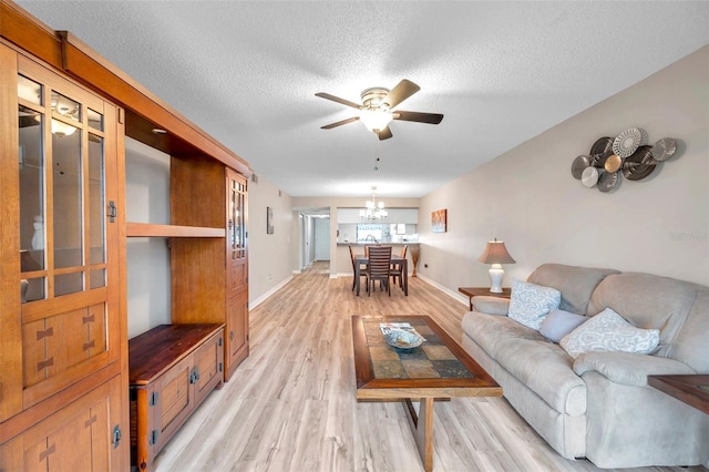 living room with light wood-type flooring, ceiling fan with notable chandelier, and a textured ceiling