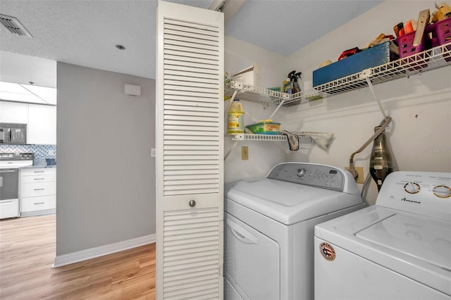 laundry room featuring a textured ceiling, light wood-type flooring, and washer and dryer