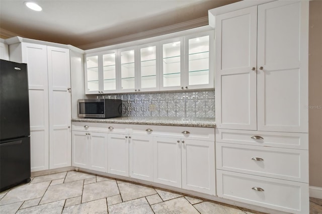 kitchen featuring stainless steel microwave, glass insert cabinets, freestanding refrigerator, and white cabinets