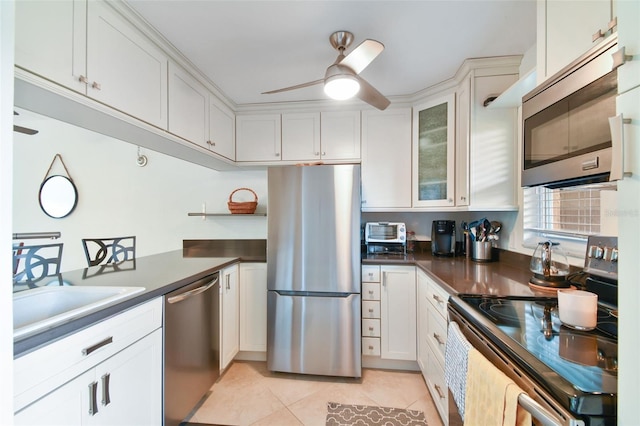 kitchen with light tile patterned floors, appliances with stainless steel finishes, glass insert cabinets, a sink, and ceiling fan