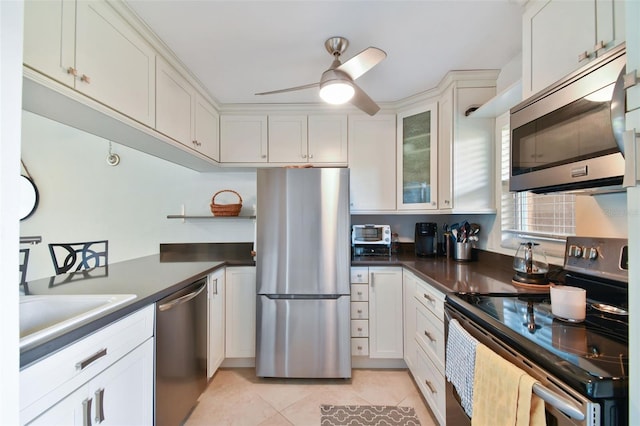 kitchen with light tile patterned floors, dark countertops, appliances with stainless steel finishes, a ceiling fan, and white cabinets