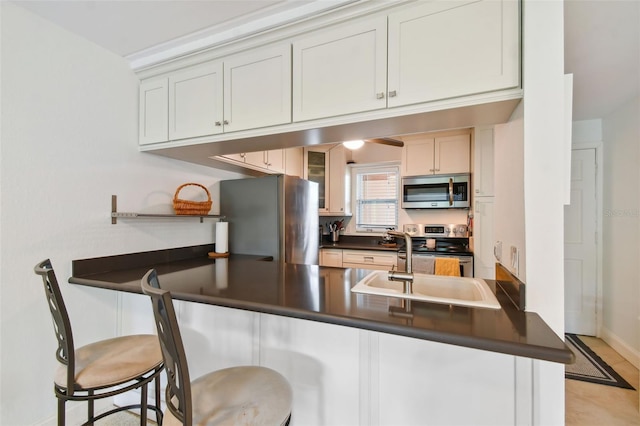 kitchen with dark countertops, appliances with stainless steel finishes, a sink, a peninsula, and a kitchen breakfast bar