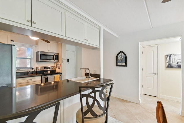 kitchen featuring light tile patterned floors, baseboards, dark countertops, appliances with stainless steel finishes, and a sink