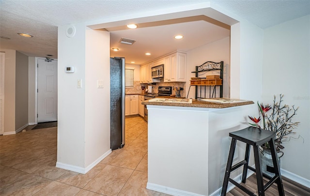 kitchen with light tile patterned floors, appliances with stainless steel finishes, kitchen peninsula, a kitchen breakfast bar, and decorative backsplash