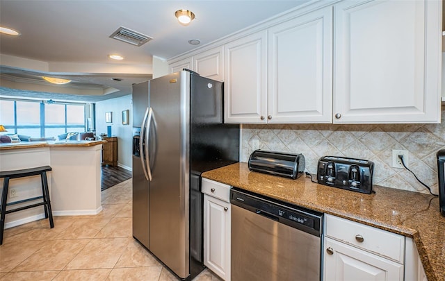 kitchen featuring appliances with stainless steel finishes, dark stone counters, white cabinetry, and light tile patterned flooring