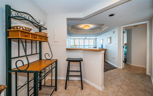 kitchen with ornamental molding, a raised ceiling, kitchen peninsula, and light tile patterned flooring