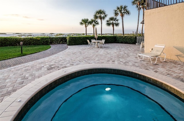 pool at dusk featuring an in ground hot tub and a patio