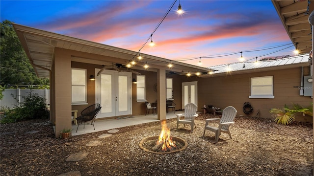 back house at dusk with an outdoor fire pit, french doors, and a patio