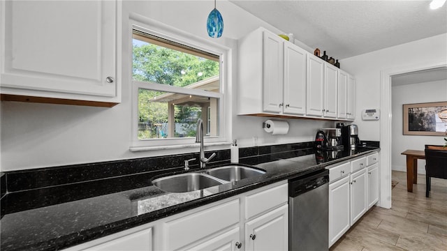 kitchen with stainless steel dishwasher, dark stone countertops, a healthy amount of sunlight, and white cabinetry