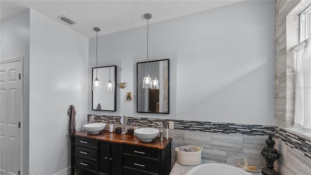 bathroom with a textured ceiling, vanity, and tile walls