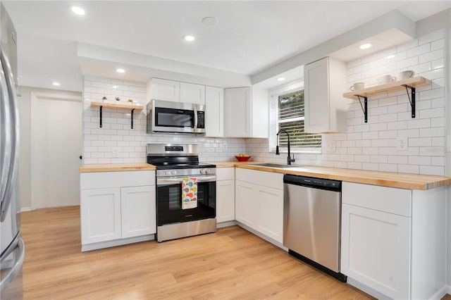 kitchen with wood counters, white cabinets, sink, light hardwood / wood-style flooring, and stainless steel appliances