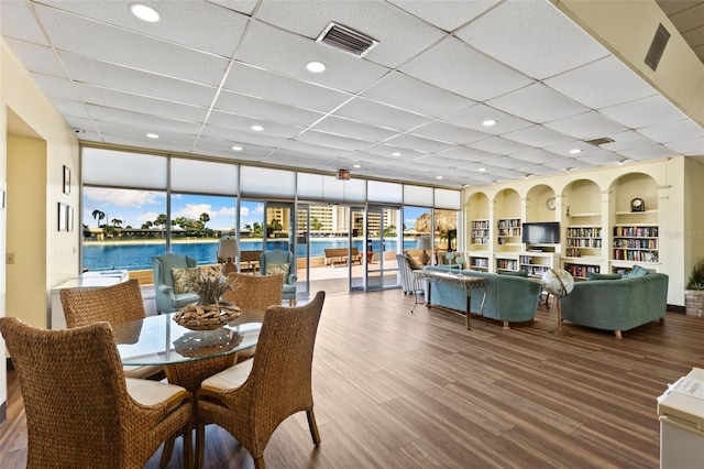 dining space with a water view, a paneled ceiling, floor to ceiling windows, and wood-type flooring