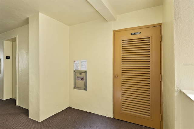 hall with elevator, beam ceiling, and dark carpet