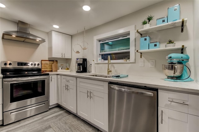 kitchen featuring stainless steel appliances, wall chimney range hood, light stone counters, white cabinets, and light hardwood / wood-style floors