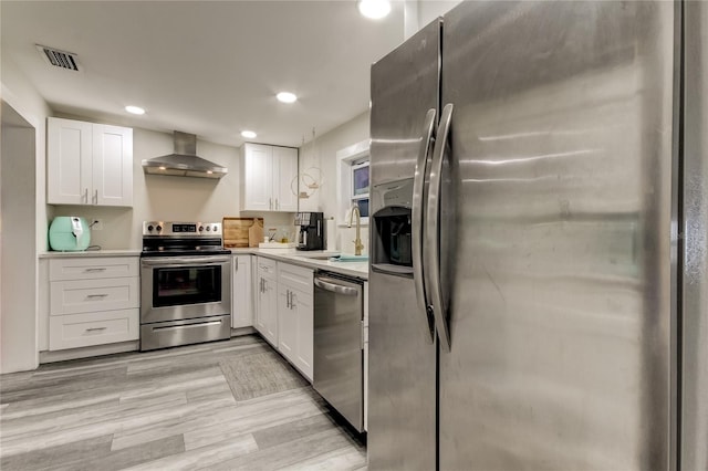 kitchen featuring wall chimney exhaust hood, appliances with stainless steel finishes, light hardwood / wood-style floors, sink, and white cabinetry