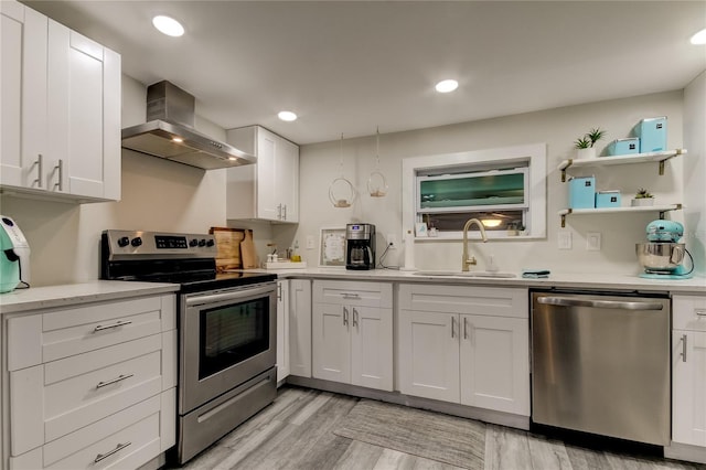 kitchen featuring wall chimney exhaust hood, appliances with stainless steel finishes, white cabinetry, and light hardwood / wood-style flooring