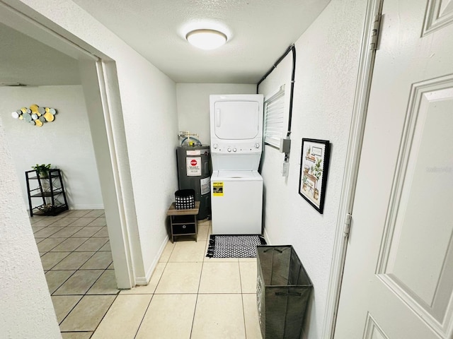 interior space featuring water heater, light tile patterned floors, a textured ceiling, and stacked washing maching and dryer